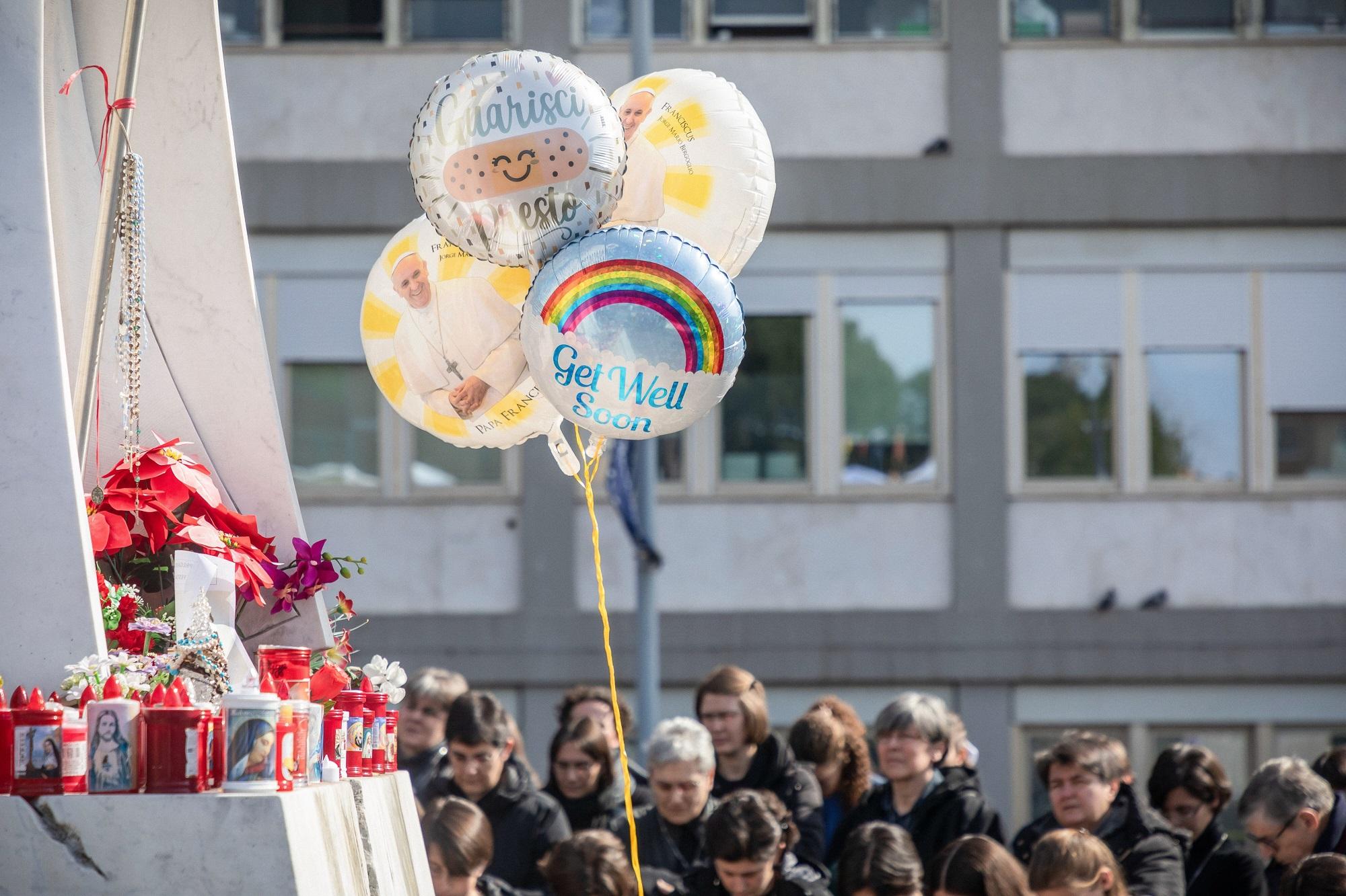 Menschen mit Votivkerzen, Luftballons, Glückwunschkarten und Blumen vor dem Gemelli-Krankenhaus beten für den kranken Papst Franziskus.