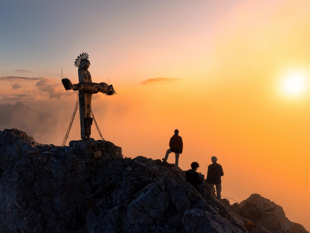 Das Gipfelkreuz in Form einer stehenden Pietà auf der Schönfeldspitze in Österreich bei Sonnenaufgang.
