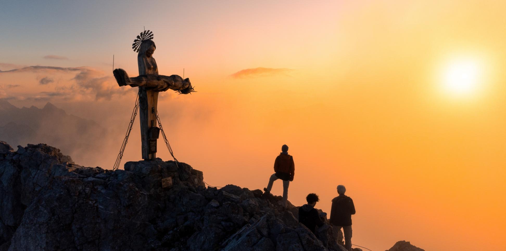 Das Gipfelkreuz in Form einer stehenden Pietà auf der Schönfeldspitze in Österreich bei Sonnenaufgang.