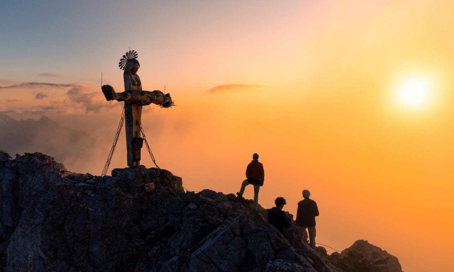 Das Gipfelkreuz in Form einer stehenden Pietà auf der Schönfeldspitze in Österreich bei Sonnenaufgang.