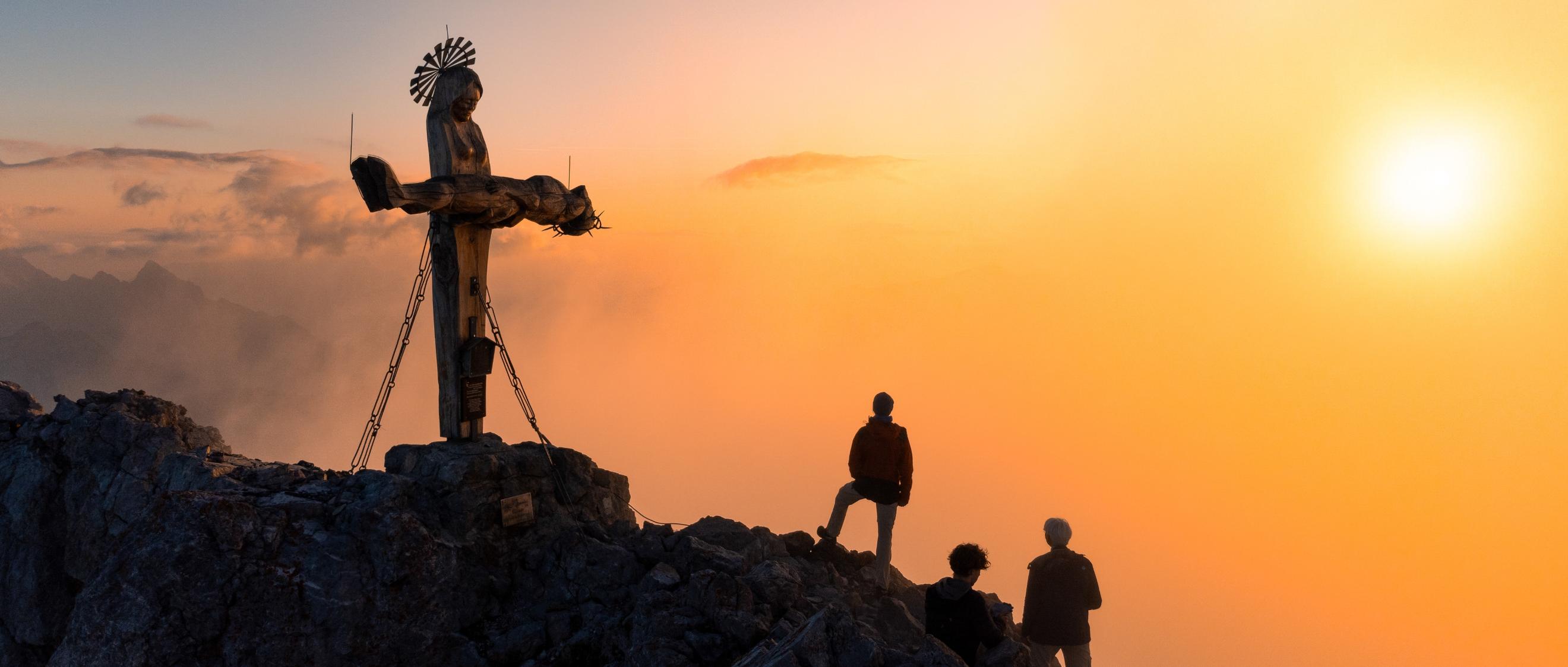 Das Gipfelkreuz in Form einer stehenden Pietà auf der Schönfeldspitze in Österreich bei Sonnenaufgang.