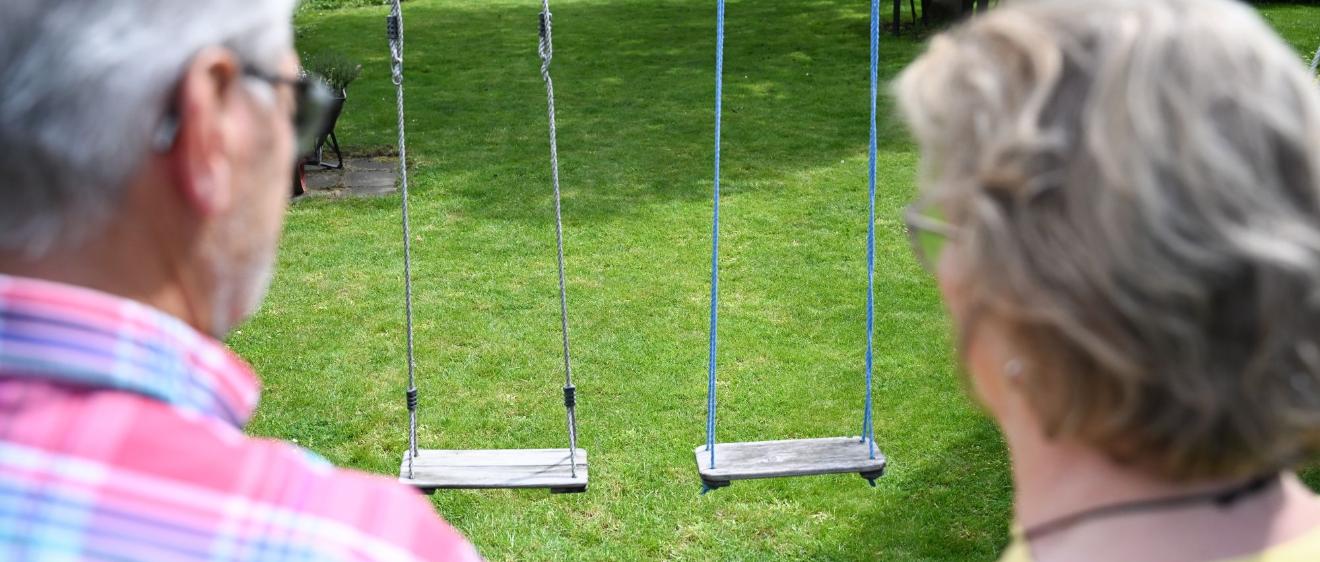 Zwei Personen von hinten gezeigt schauen auf eine leere Schaukel