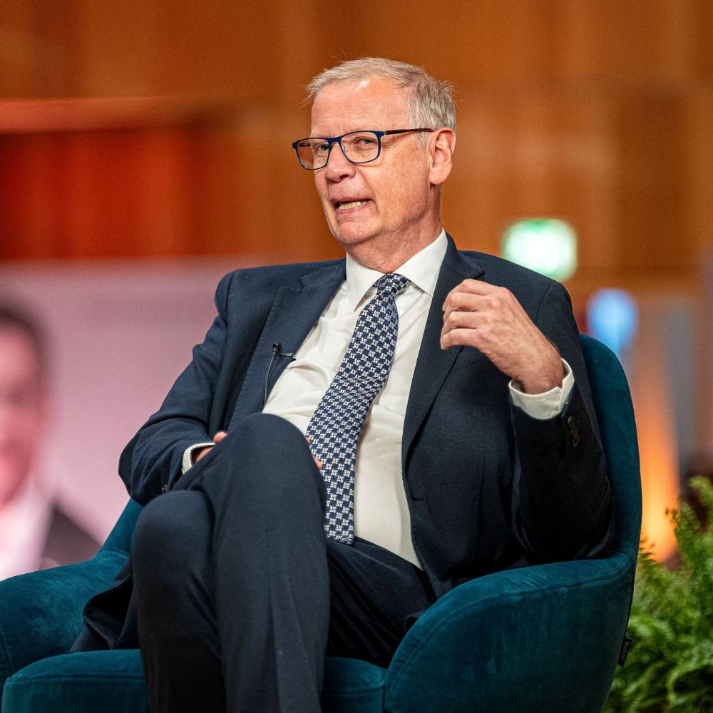 Ein Mann mit Krawatte sitzt in einem Sessel und spricht