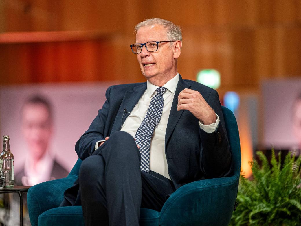 Ein Mann mit Krawatte sitzt in einem Sessel und spricht