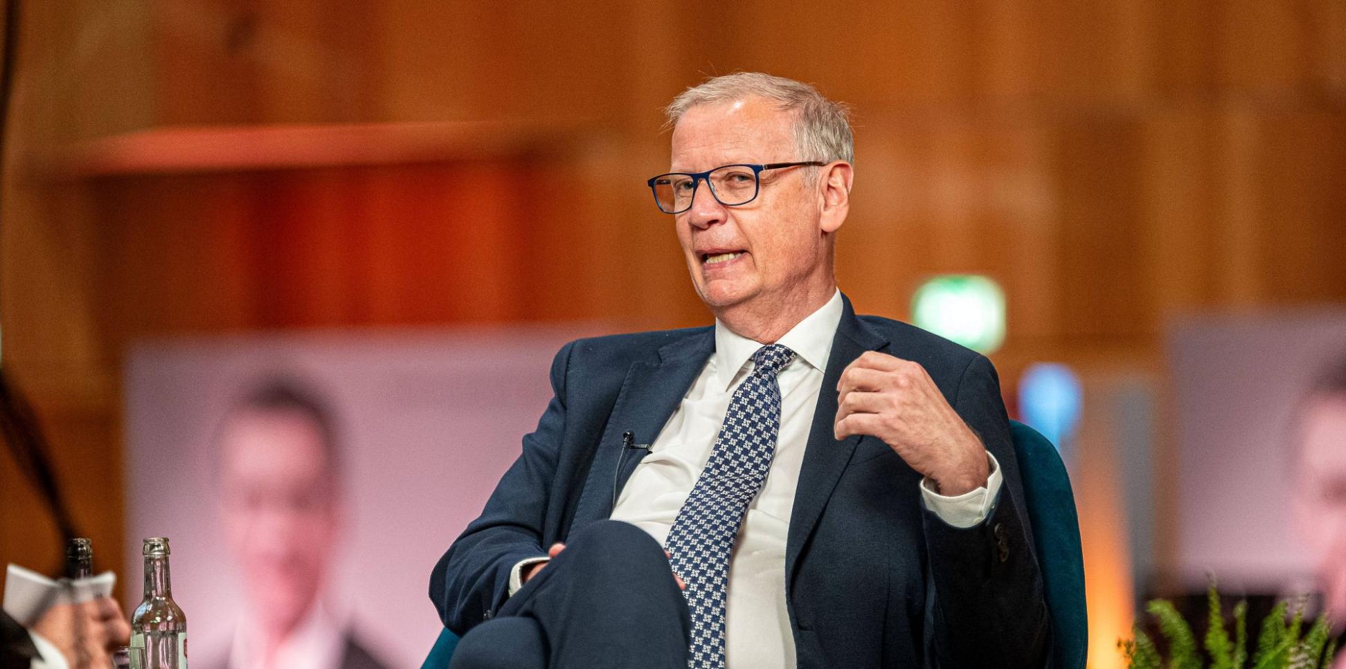 Ein Mann mit Krawatte sitzt in einem Sessel und spricht