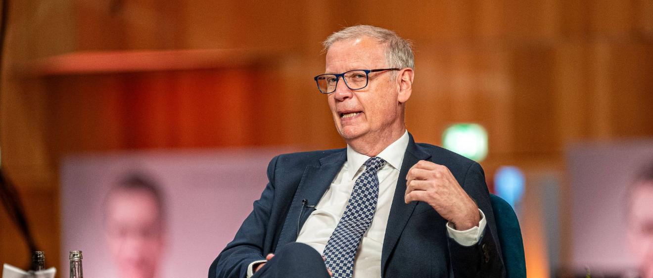 Ein Mann mit Krawatte sitzt in einem Sessel und spricht