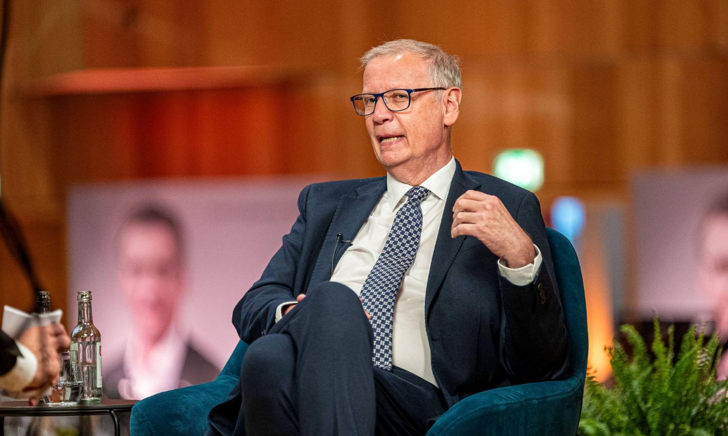 Ein Mann mit Krawatte sitzt in einem Sessel und spricht