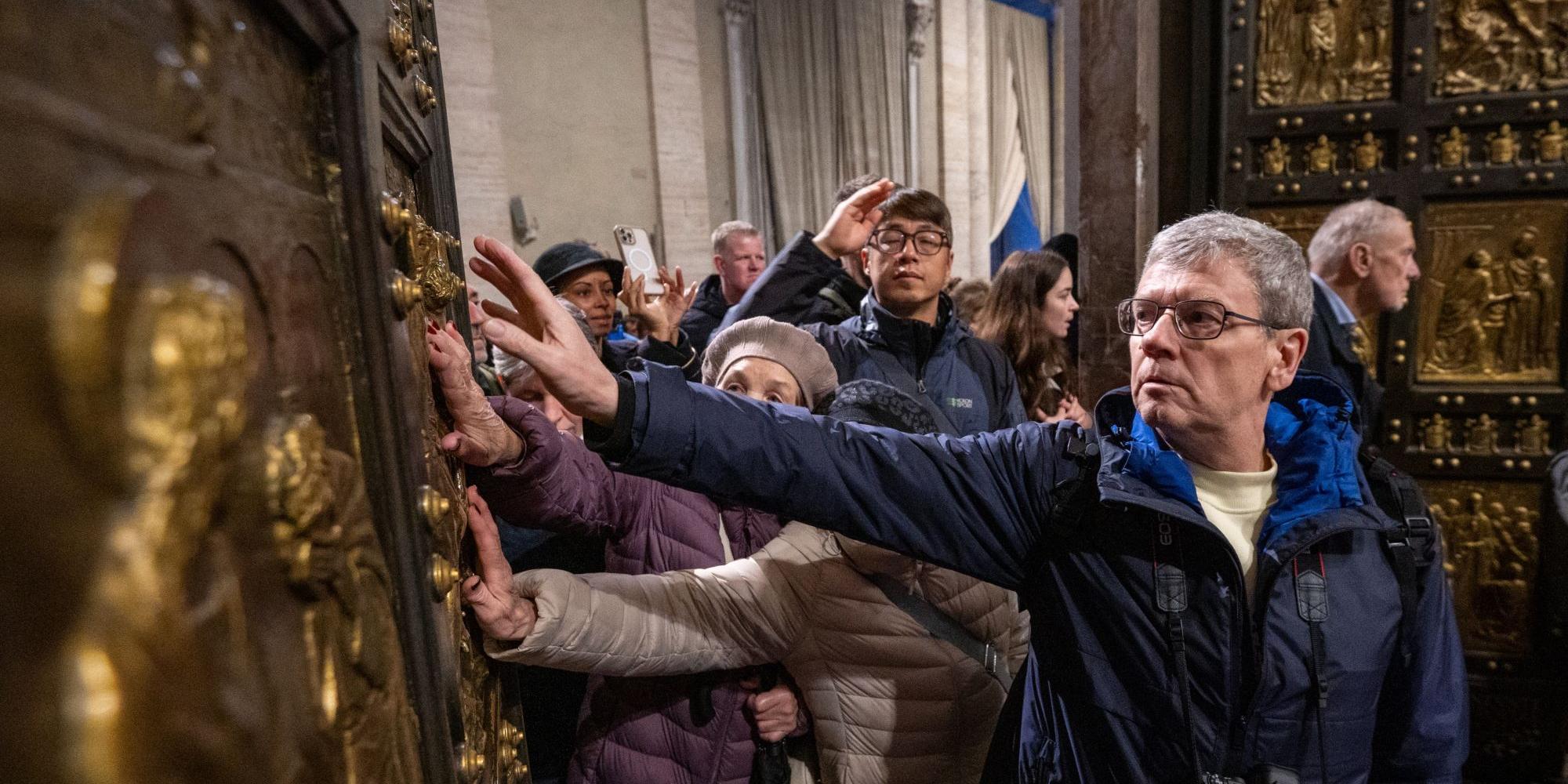 Pilger berühren beim Durchschreiten die Heilige Pforte im Petersdom im Vatikan.