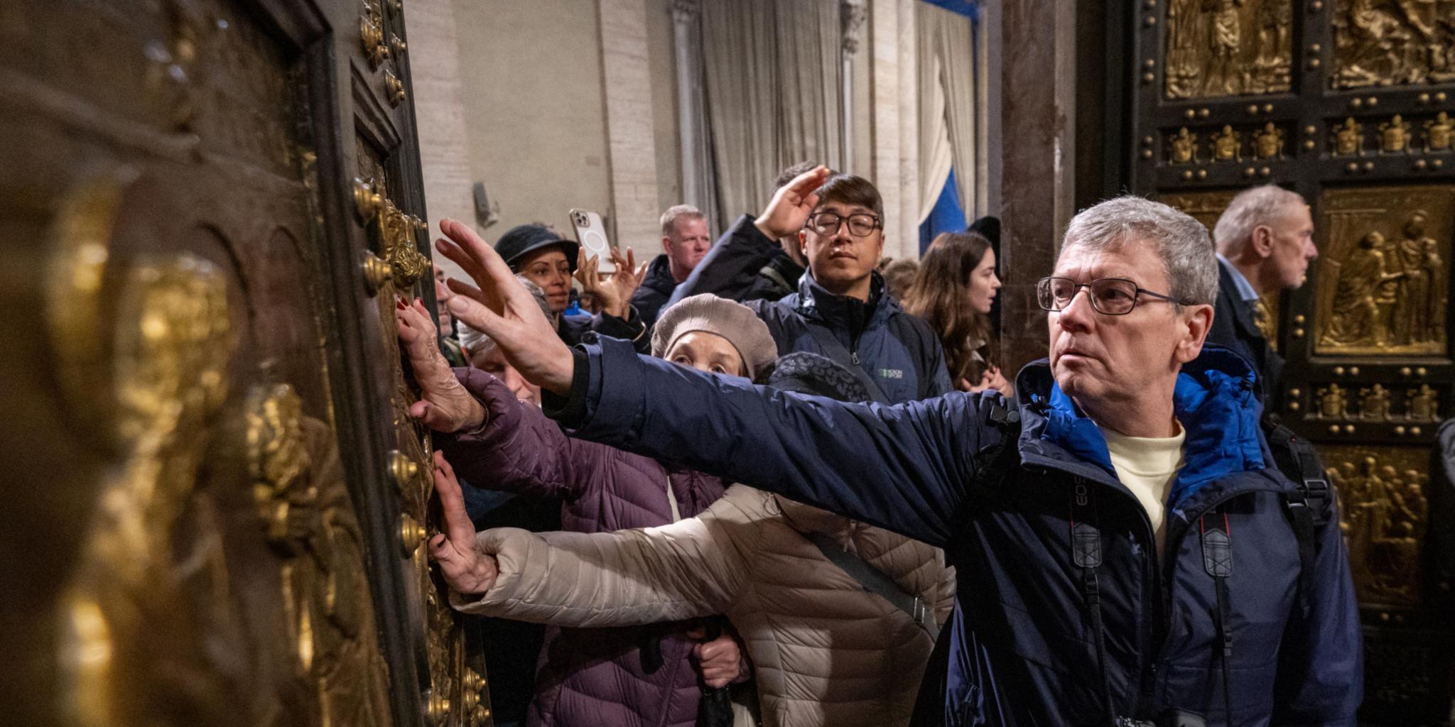 Pilger berühren beim Durchschreiten die Heilige Pforte im Petersdom im Vatikan.