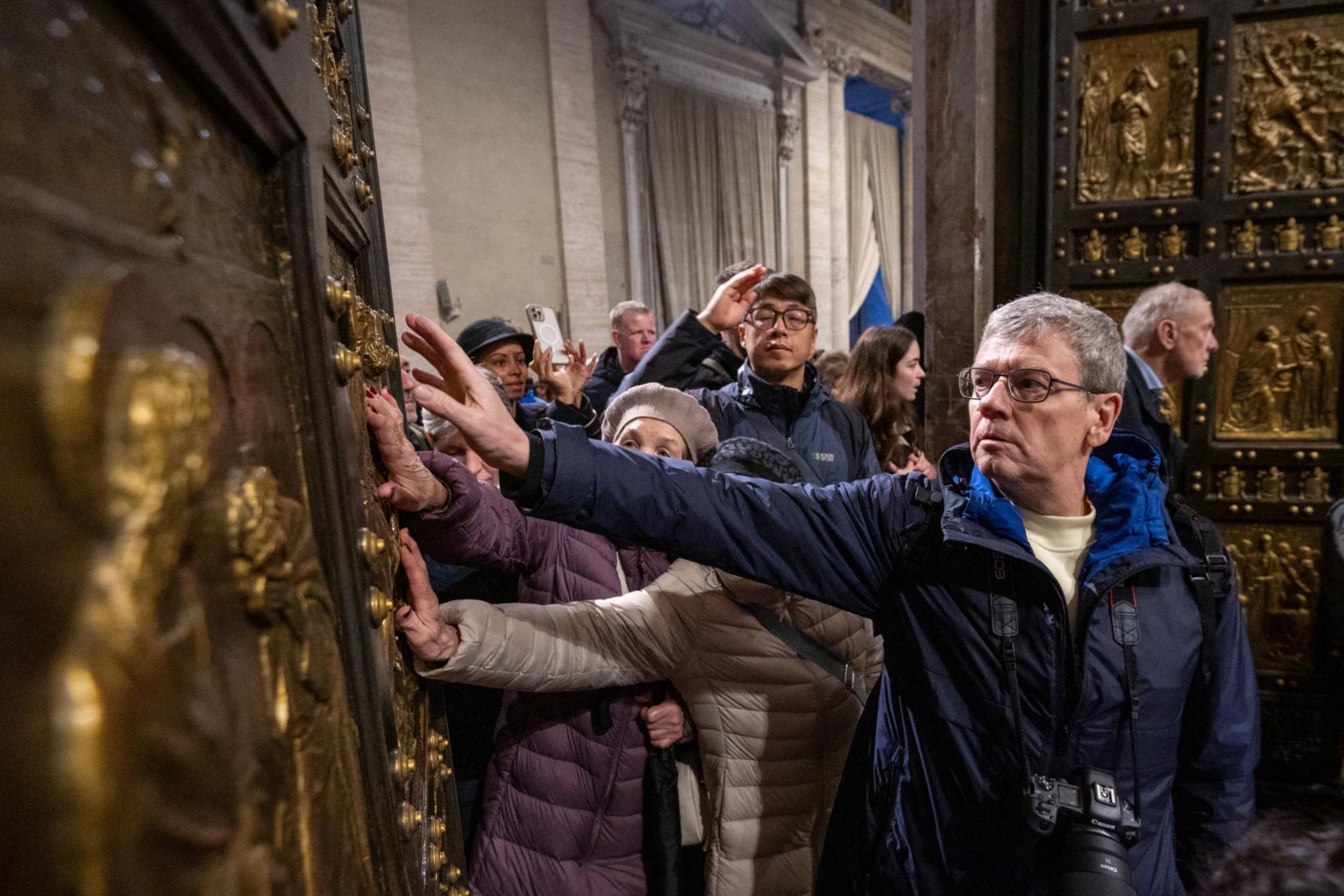 Pilger berühren beim Durchschreiten die Heilige Pforte im Petersdom im Vatikan.
