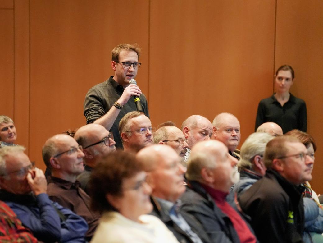 Ein Mann steht in einer Gruppe von Menschen und hält ein Mikrofon in der Hand