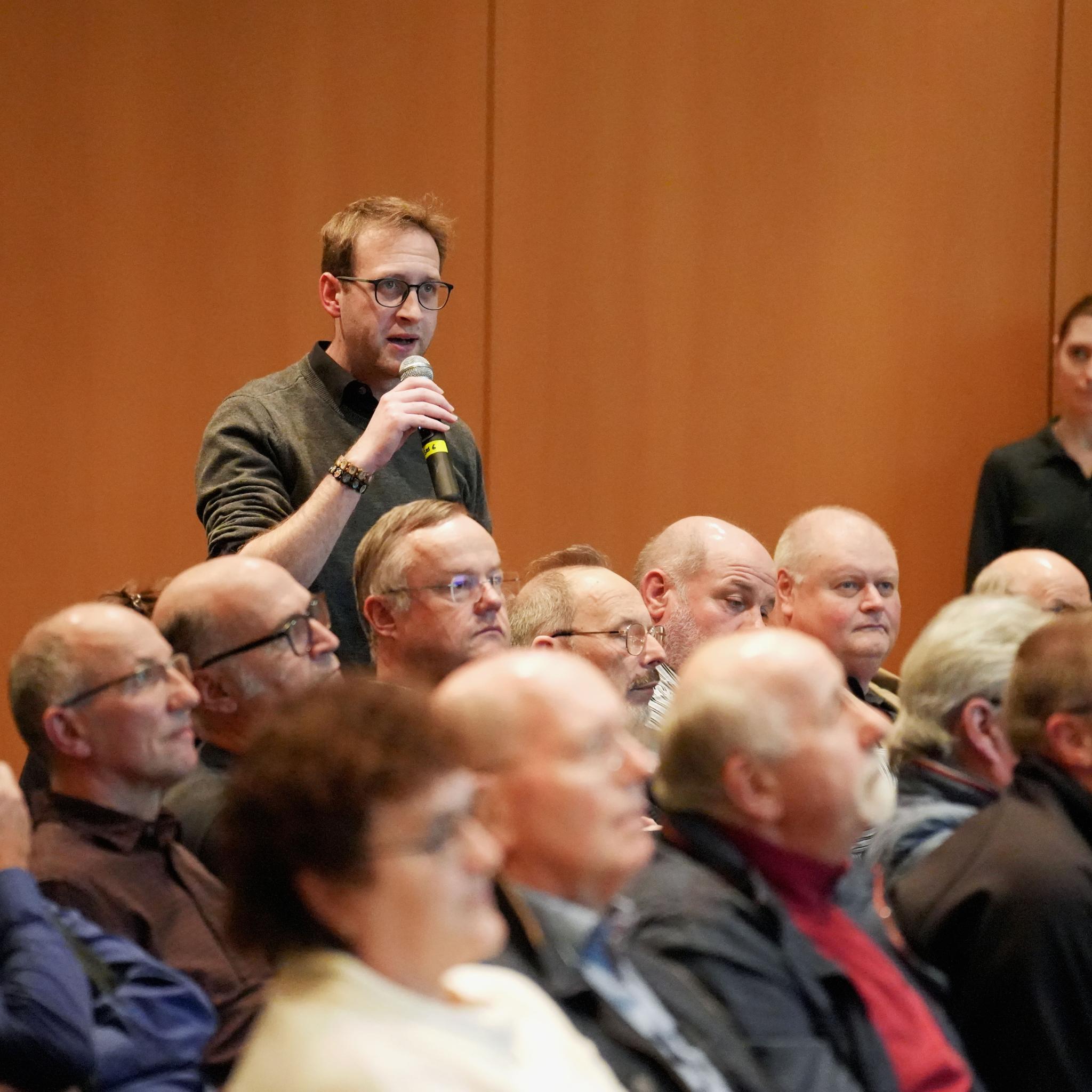 Ein Mann steht in einer Gruppe von Menschen und hält ein Mikrofon in der Hand