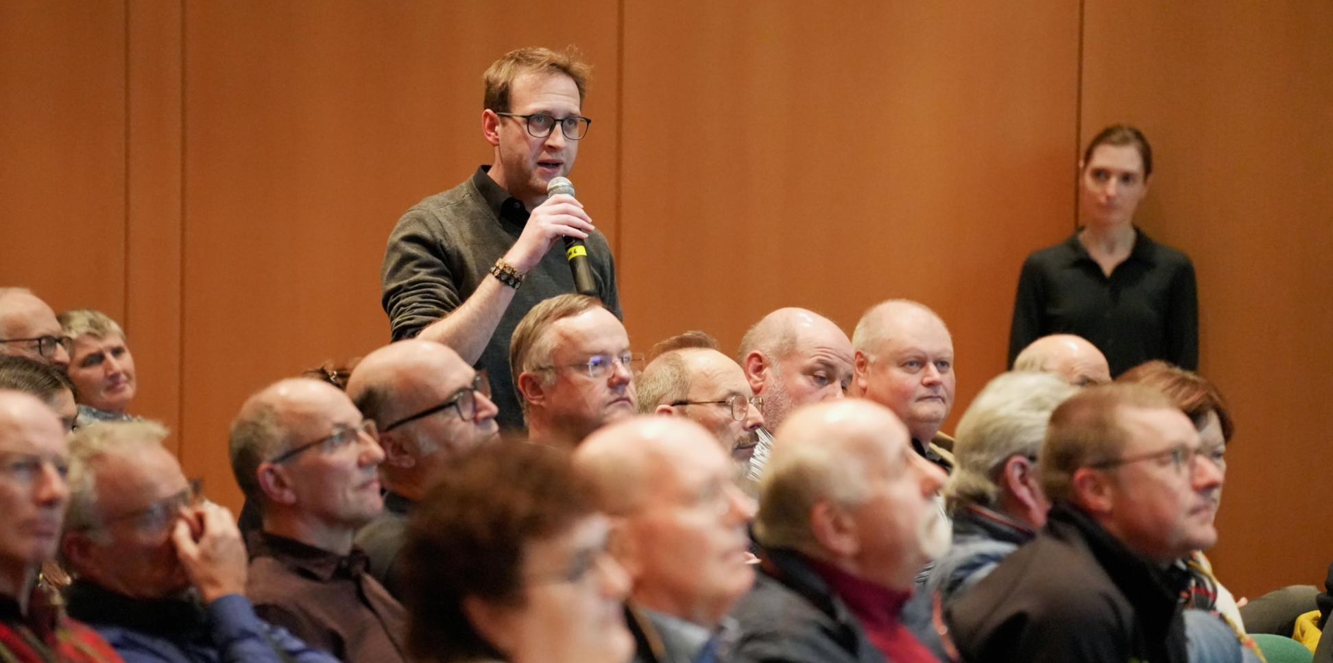 Ein Mann steht in einer Gruppe von Menschen und hält ein Mikrofon in der Hand