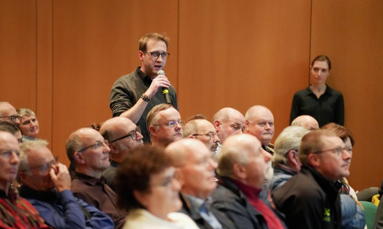 Ein Mann steht in einer Gruppe von Menschen und hält ein Mikrofon in der Hand