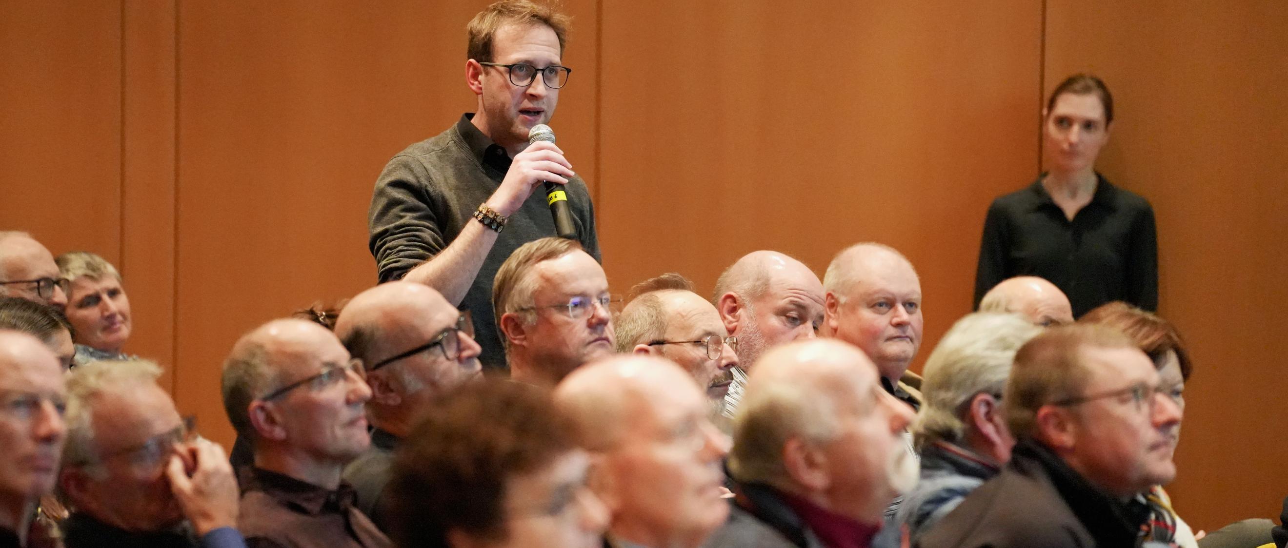 Ein Mann steht in einer Gruppe von Menschen und hält ein Mikrofon in der Hand