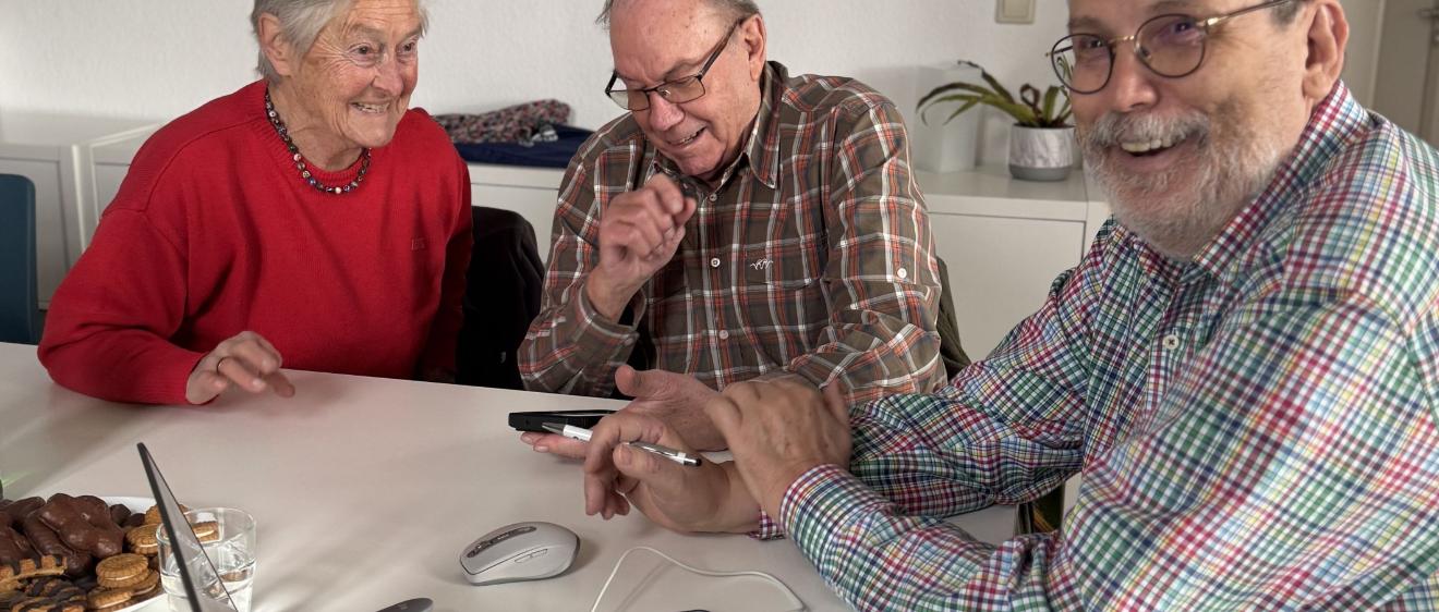 Zwei Teilnehmer gemeinsam mit Ingo Neumann (rechts) mit digitalen Geräten an einem Tisch.