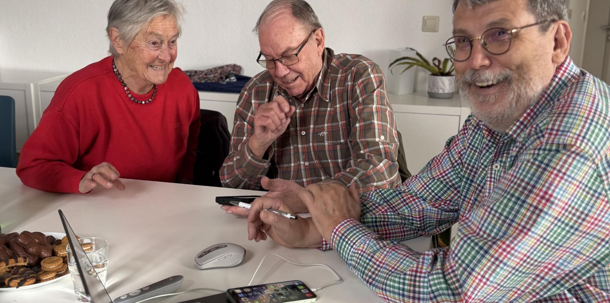 Zwei Teilnehmer gemeinsam mit Ingo Neumann (rechts) mit digitalen Geräten an einem Tisch.