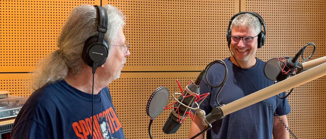 Zwei Männer mit Kopfhörern vor Mikrofonen unterhalten sich