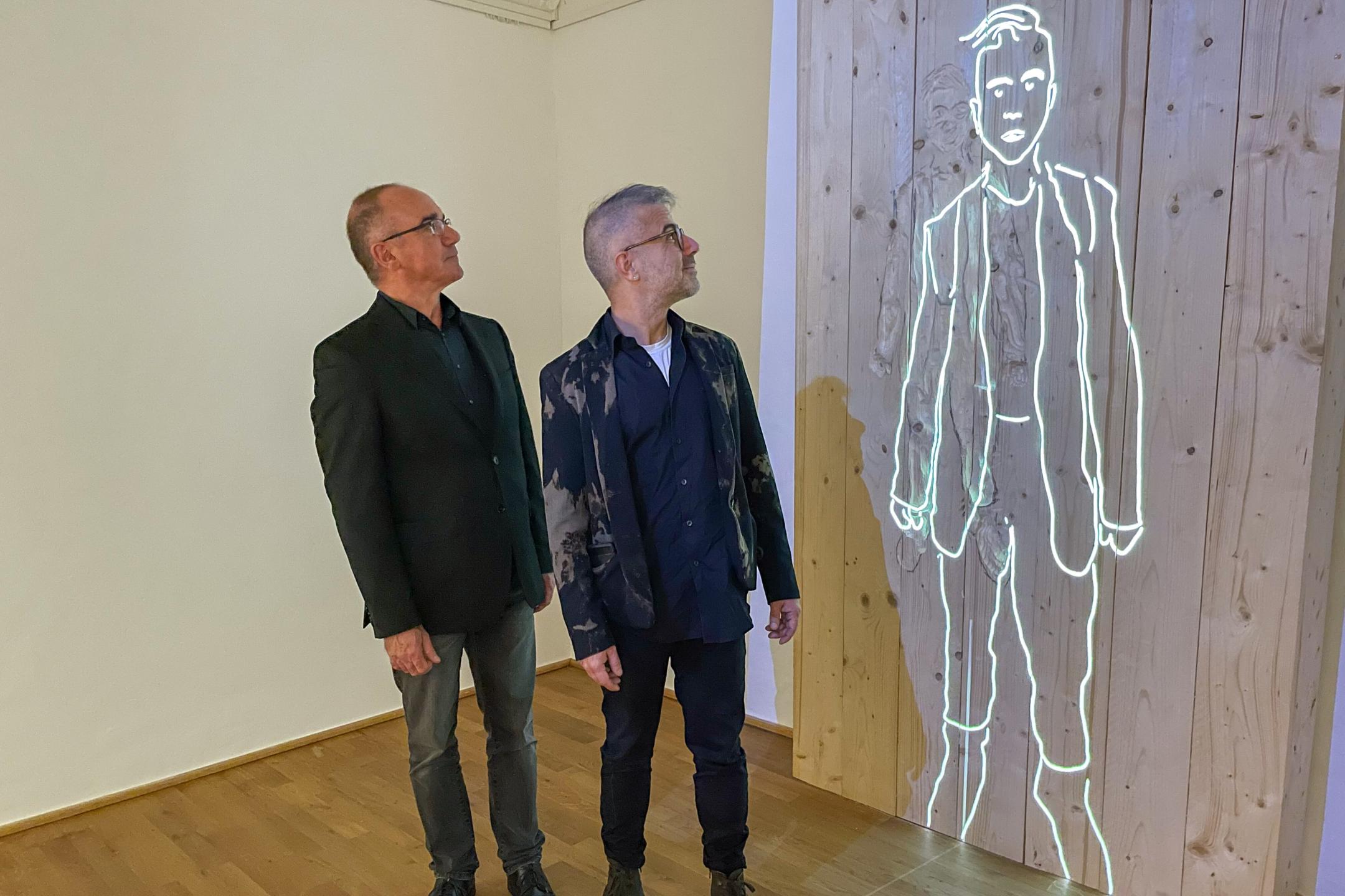 Medienkünstler Burkhard Detzler (links) und Mert Akbal blicken auf die von ihnen mit KI generierte Silhouette von Willi Graf in der Ausstellung.