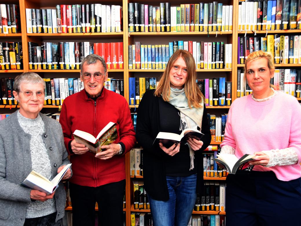 Ein Mann und drei Frauen mit Büchern in den Händen vor einem Bücherregal