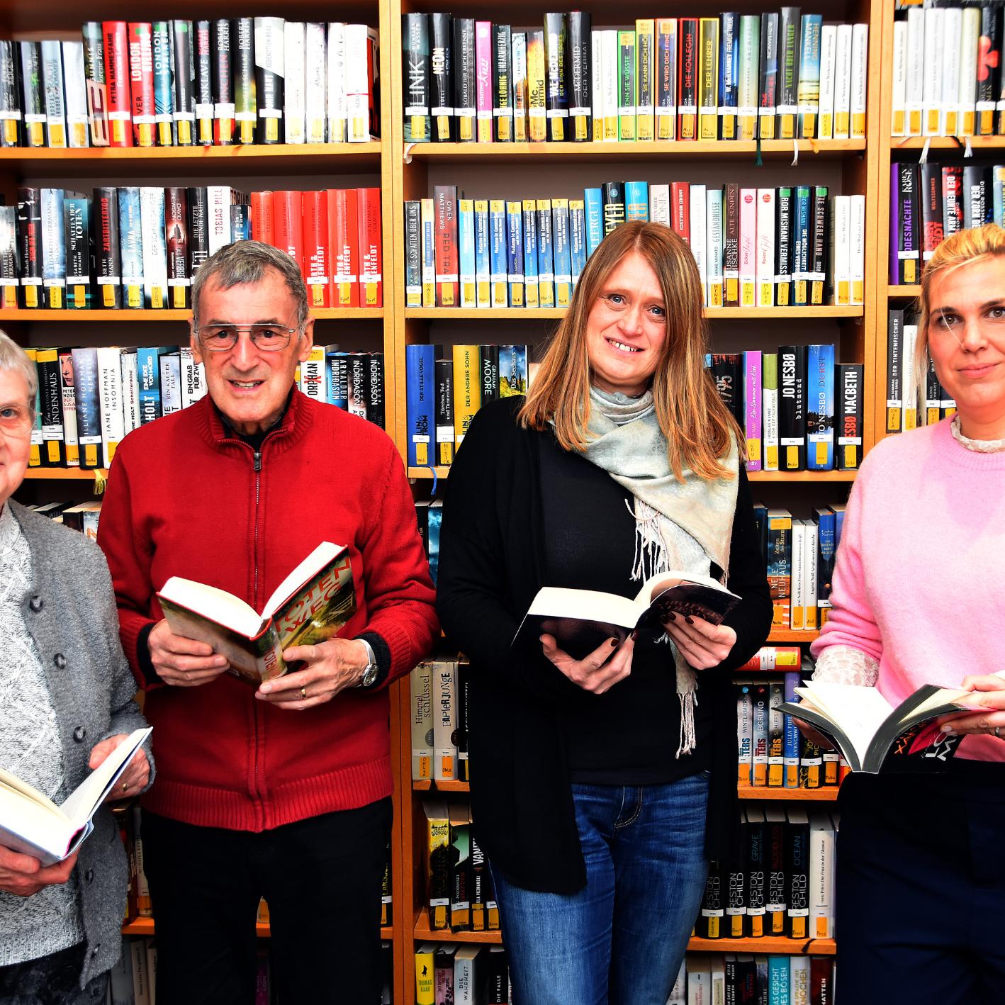 Ein Mann und drei Frauen mit Büchern in den Händen vor einem Bücherregal