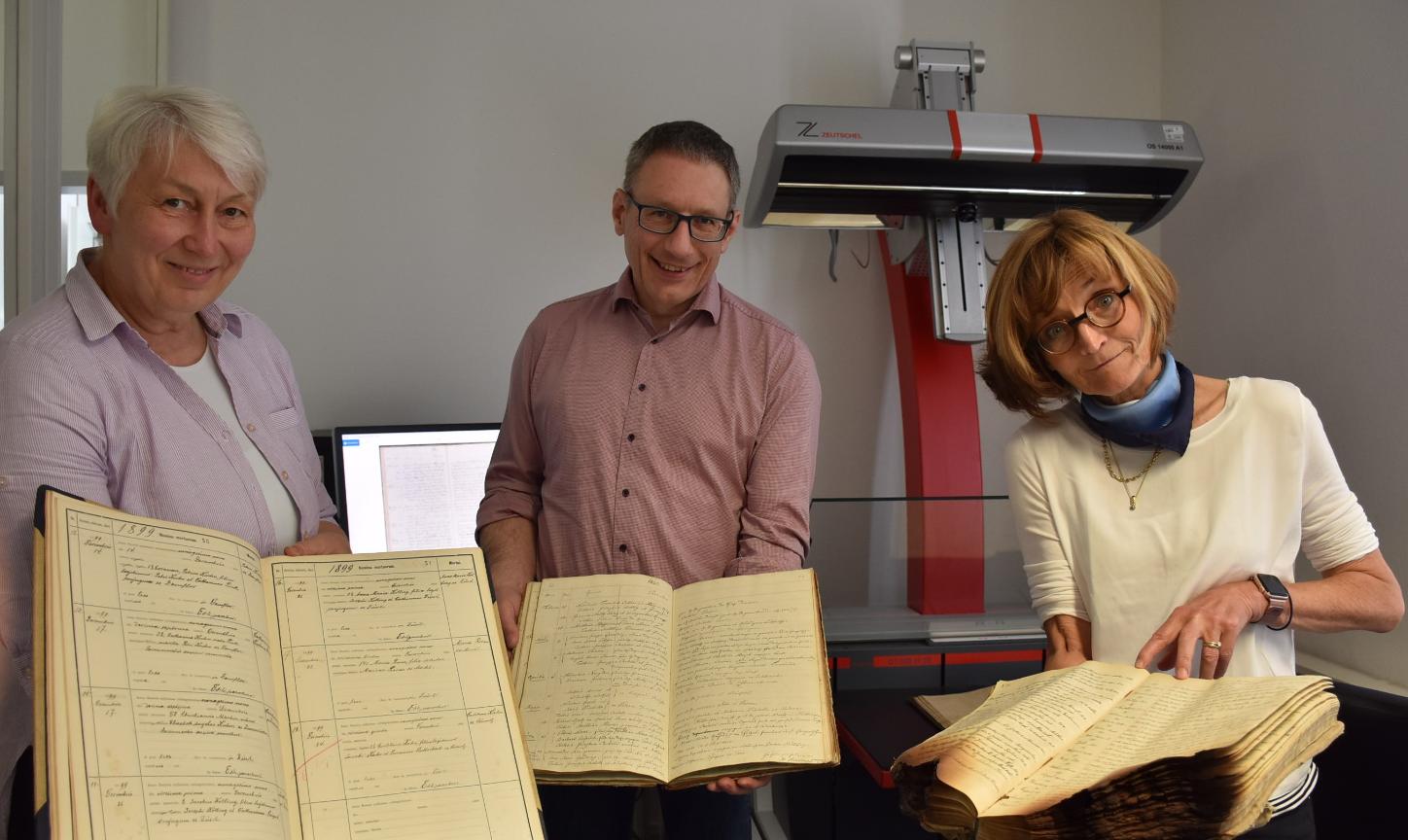 Drei der 7000 Kirchenbücher aus dem Bistum, die im Projekt digitalisiert werden, zeigen Monica Sinderhauf, Stefan Nicolay und Marita Kohl (von links).