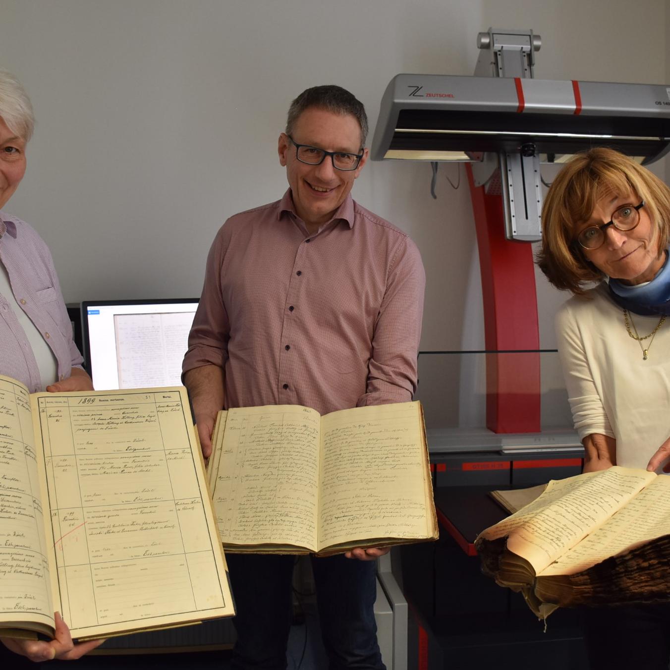 Drei der 7000 Kirchenbücher aus dem Bistum, die im Projekt digitalisiert werden, zeigen Monica Sinderhauf, Stefan Nicolay und Marita Kohl (von links).