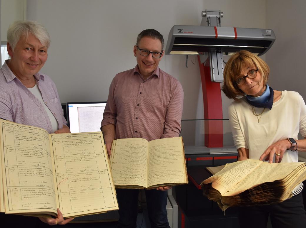 Drei der 7000 Kirchenbücher aus dem Bistum, die im Projekt digitalisiert werden, zeigen Monica Sinderhauf, Stefan Nicolay und Marita Kohl (von links).