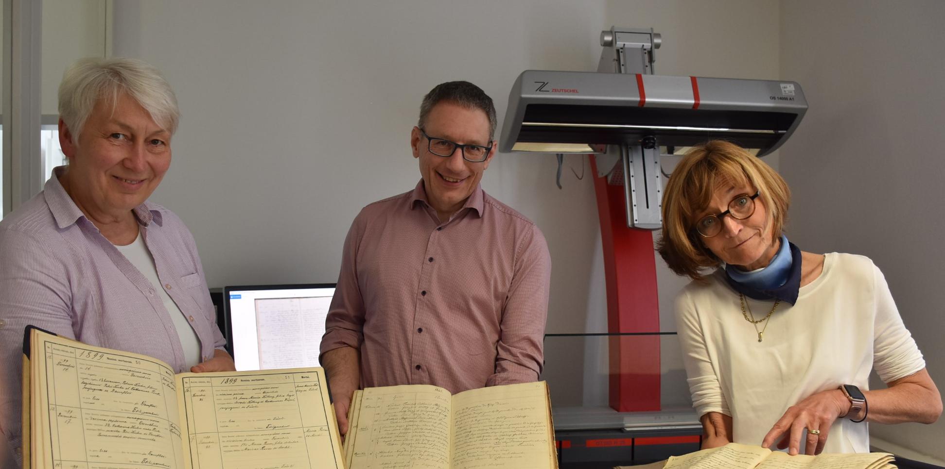 Drei der 7000 Kirchenbücher aus dem Bistum, die im Projekt digitalisiert werden, zeigen Monica Sinderhauf, Stefan Nicolay und Marita Kohl (von links).