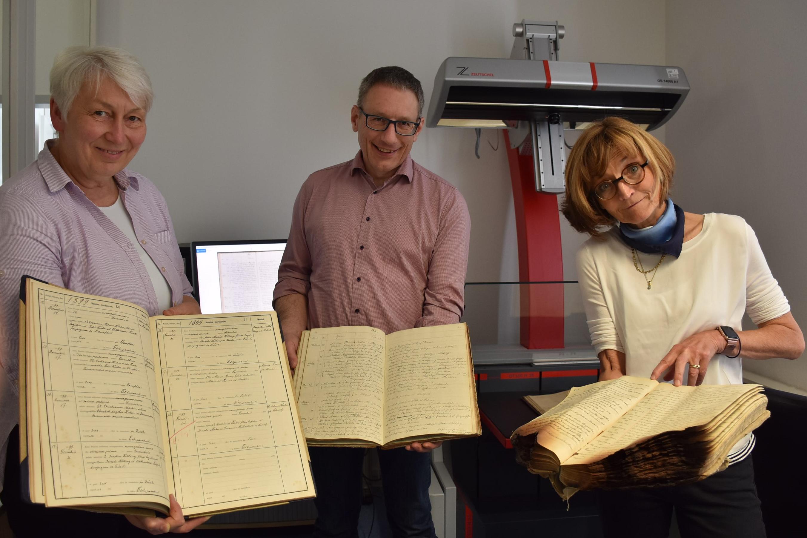 Drei Personen präsentieren Kirchenbücher