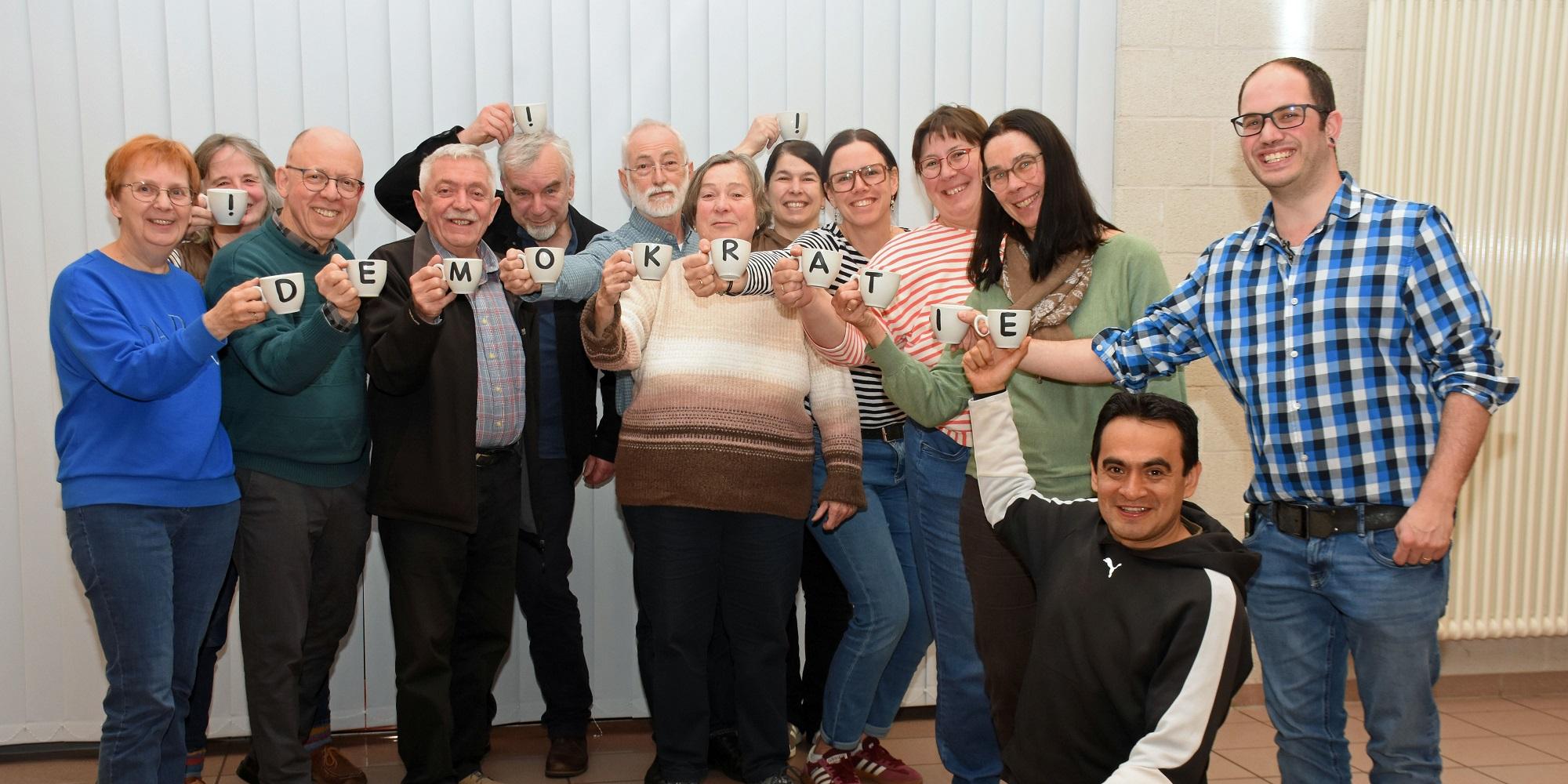 Die Mitglieder des Pfarrgemeinderates halten mit Buchstaben bedruckte Tassen, die zusammen das Wort Demokratie ergeben.