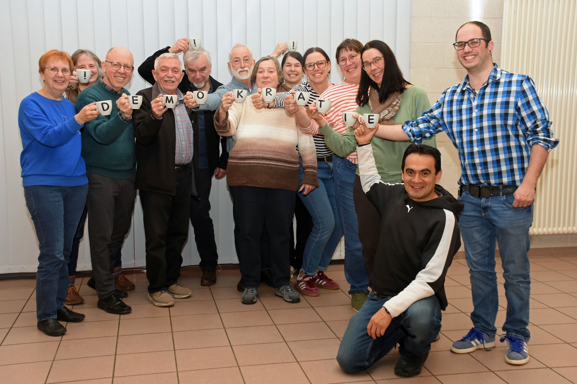 Die Mitglieder des Pfarrgemeinderates halten mit Buchstaben bedruckte Tassen, die zusammen das Wort Demokratie ergeben.