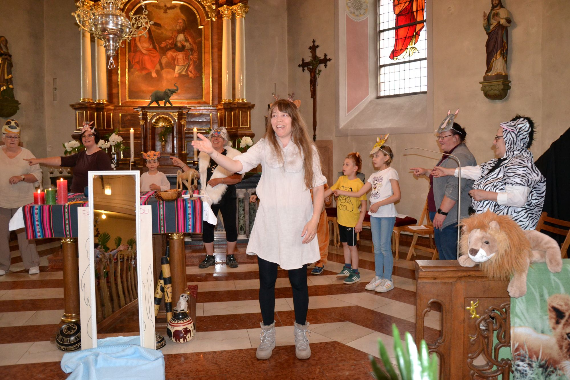 Eine Frau steht vor einem Altar und singt, drumherum Kinder in Tierkostümen
