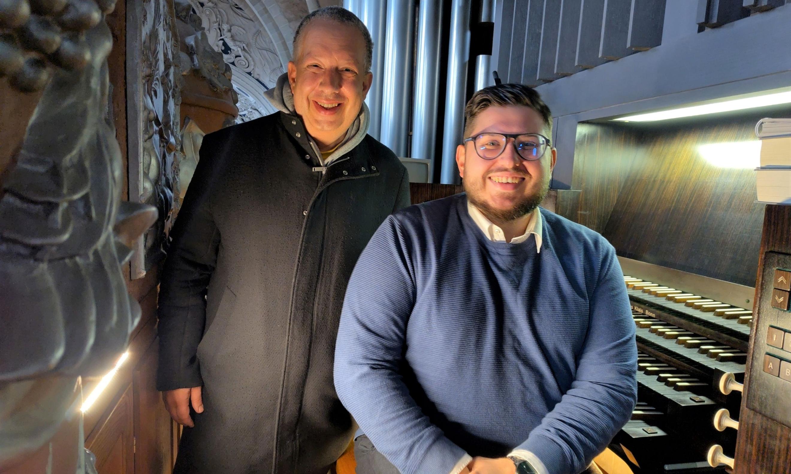Zwei Männer stehen vor einer Orgel und schauen in die Kamera