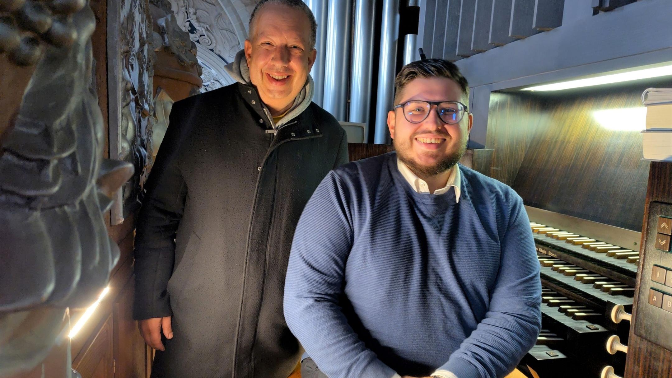 Zwei Männer stehen vor einer Orgel und schauen in die Kamera