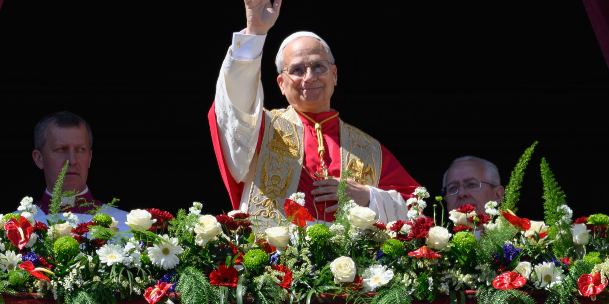 Ein Mann winkt von einem mit Blumen geschmückten Balkon