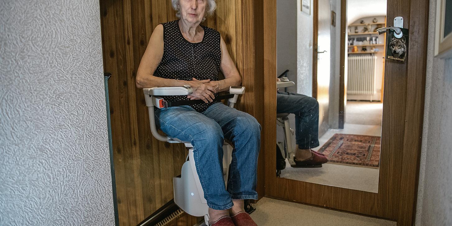 Eine Frau sitzt auf einem Treppenlift. (c) imago images Eine Frau sitzt auf einem Treppenlift.