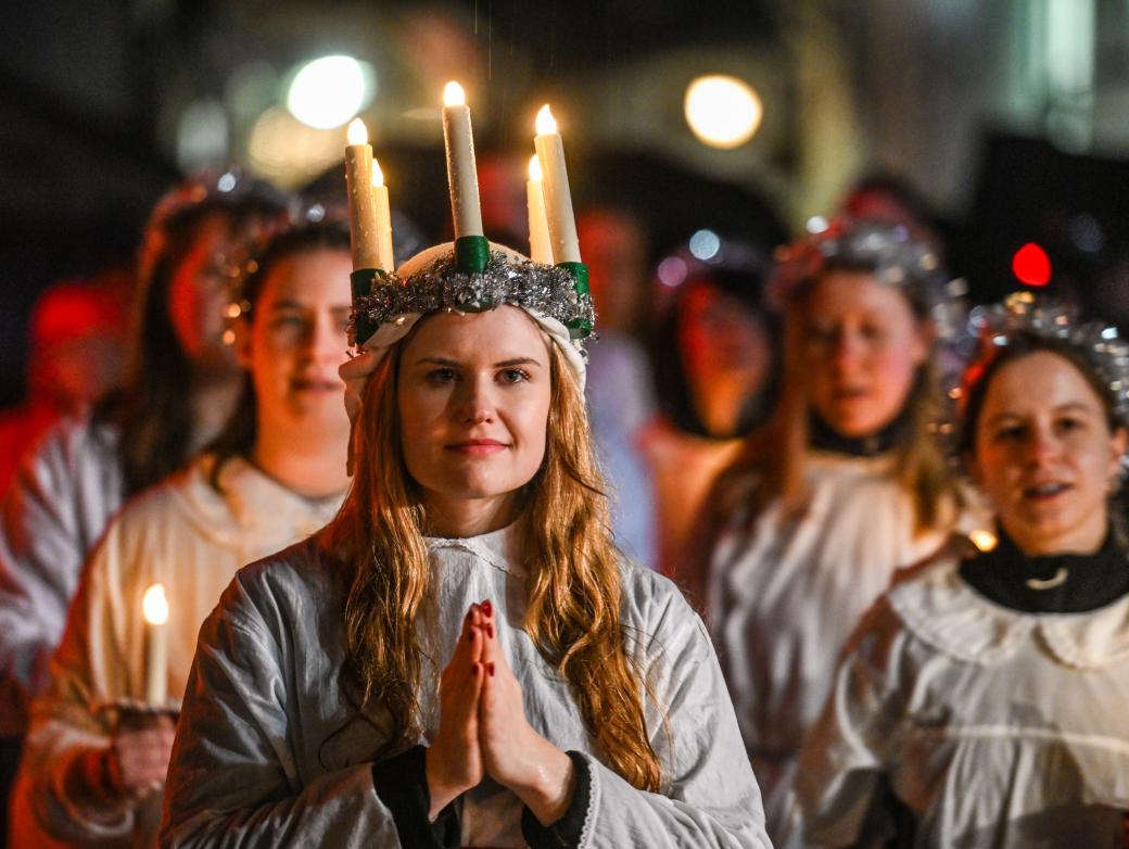 Ein Mädchen mit gefaltete Händen und einem Kranz mit brennenden Kerzen auf dem Kopf