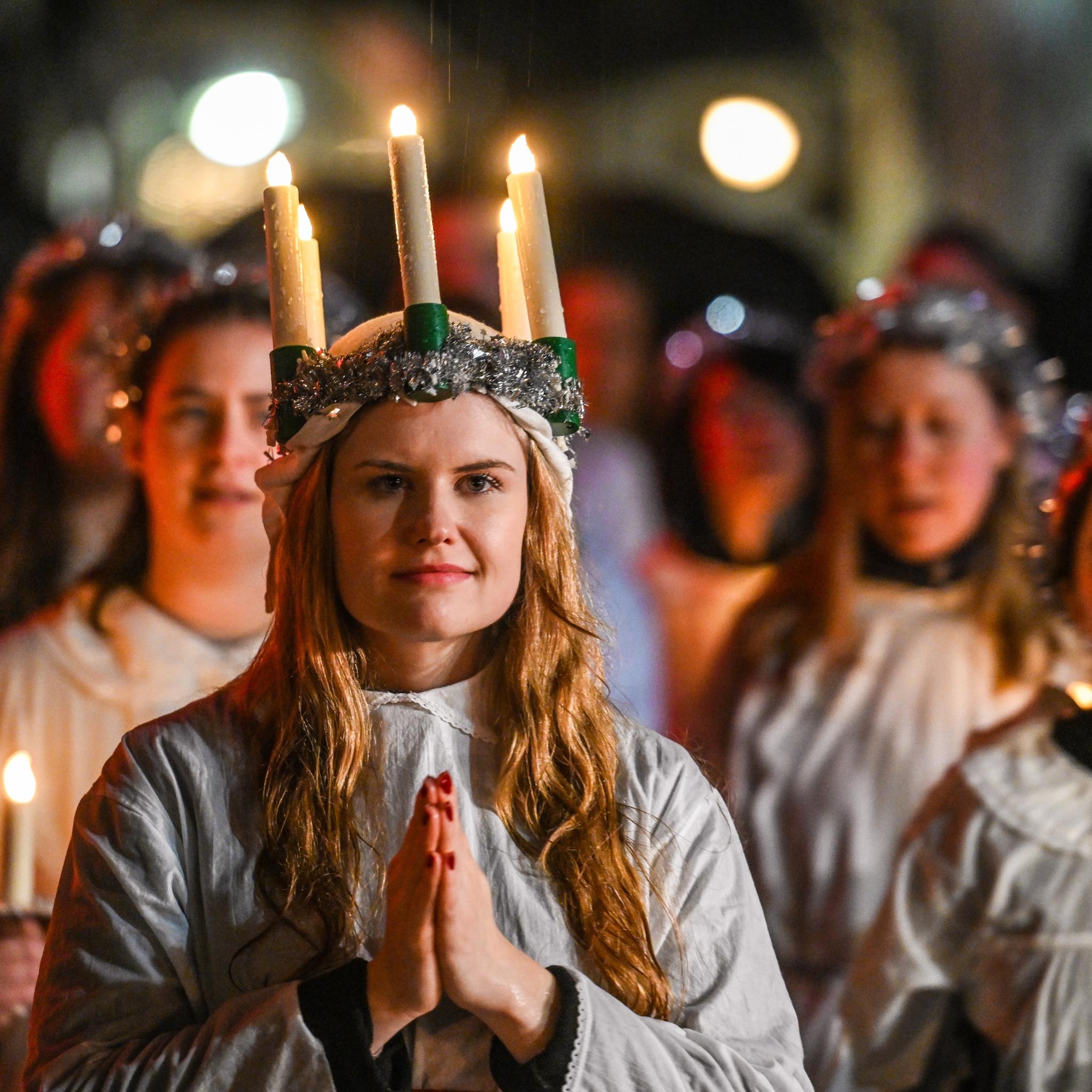 Ein Mädchen mit gefaltete Händen und einem Kranz mit brennenden Kerzen auf dem Kopf