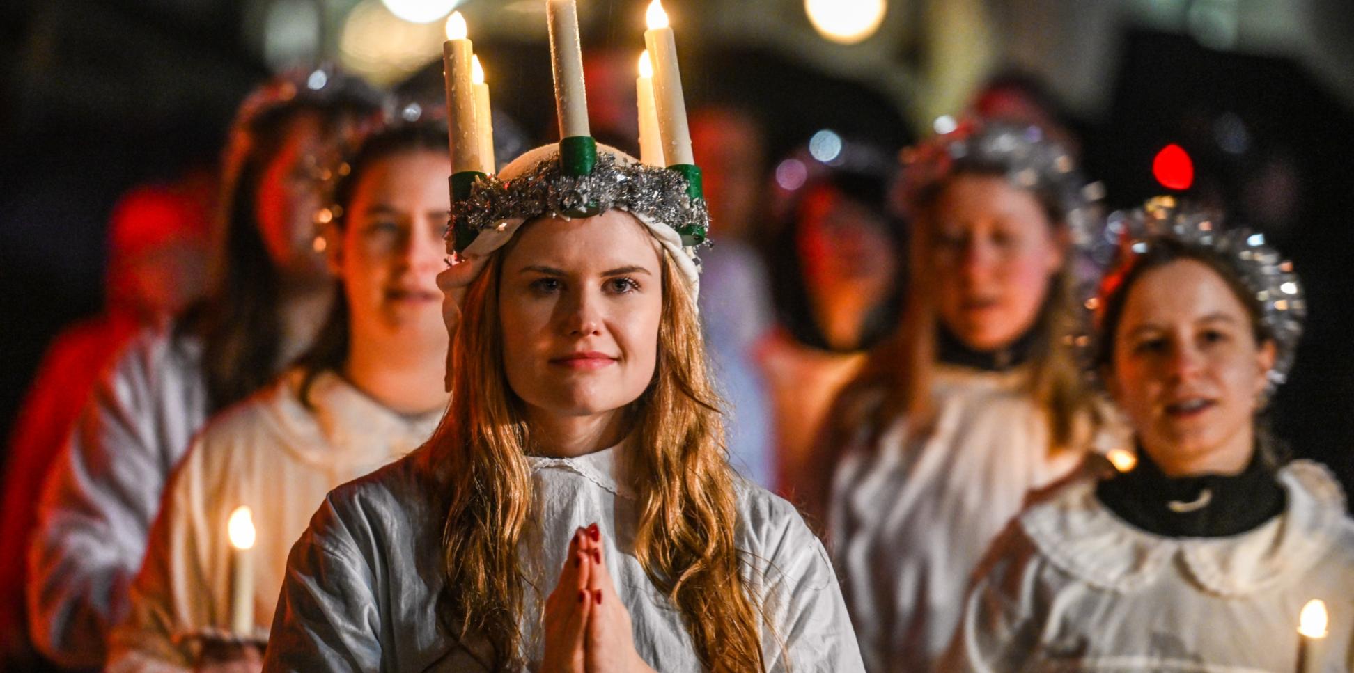 Ein Mädchen mit gefaltete Händen und einem Kranz mit brennenden Kerzen auf dem Kopf