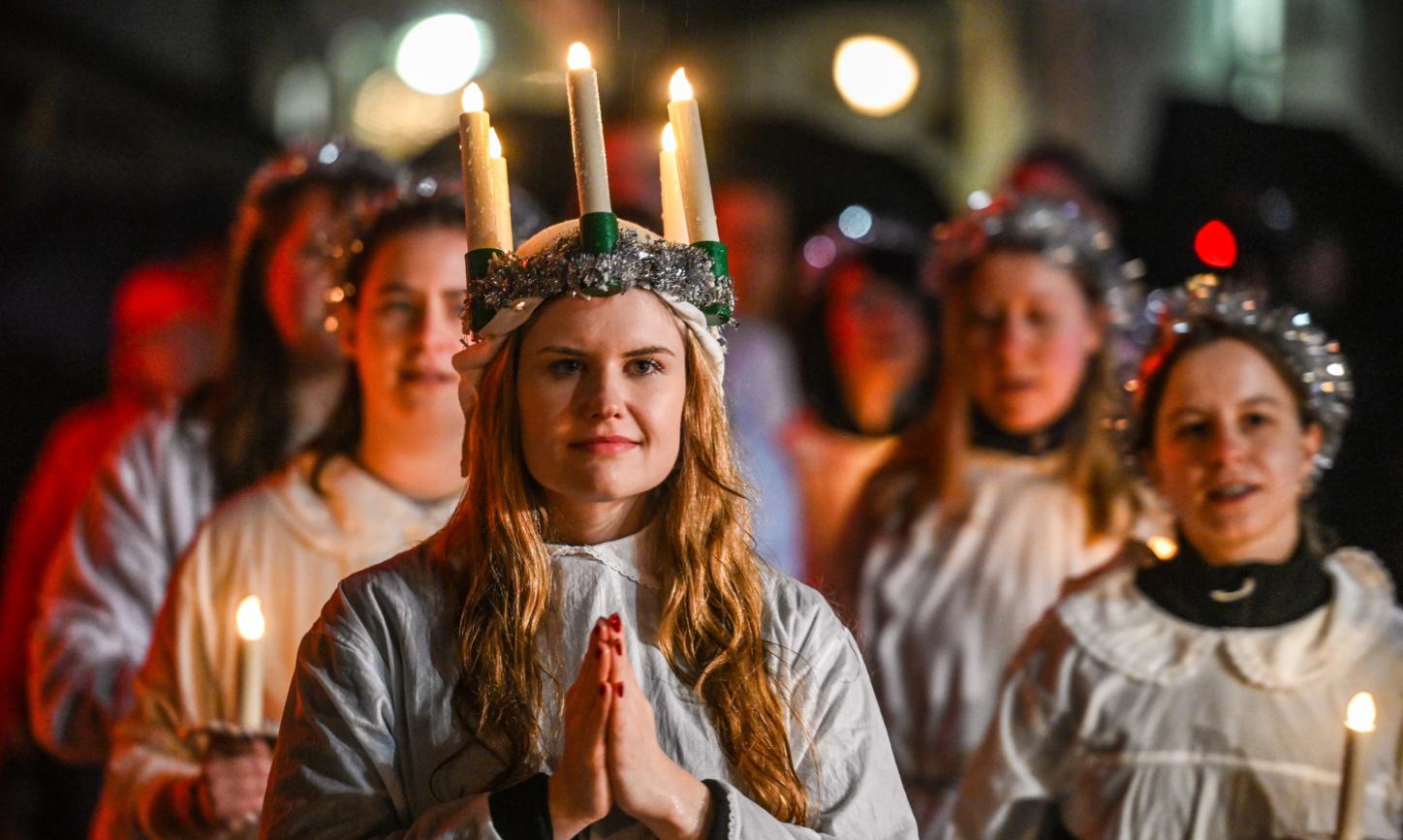 Ein Mädchen mit gefaltete Händen und einem Kranz mit brennenden Kerzen auf dem Kopf