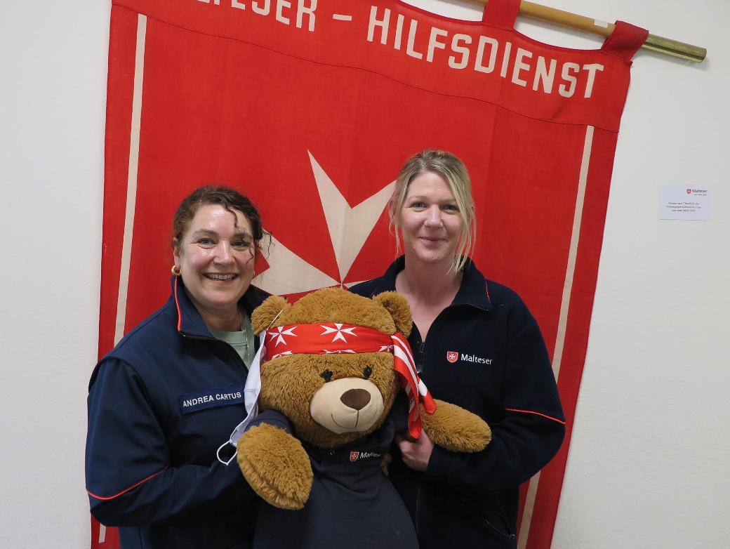 Zwei Frauen in Malteser-Jacken halten einen Teddybär