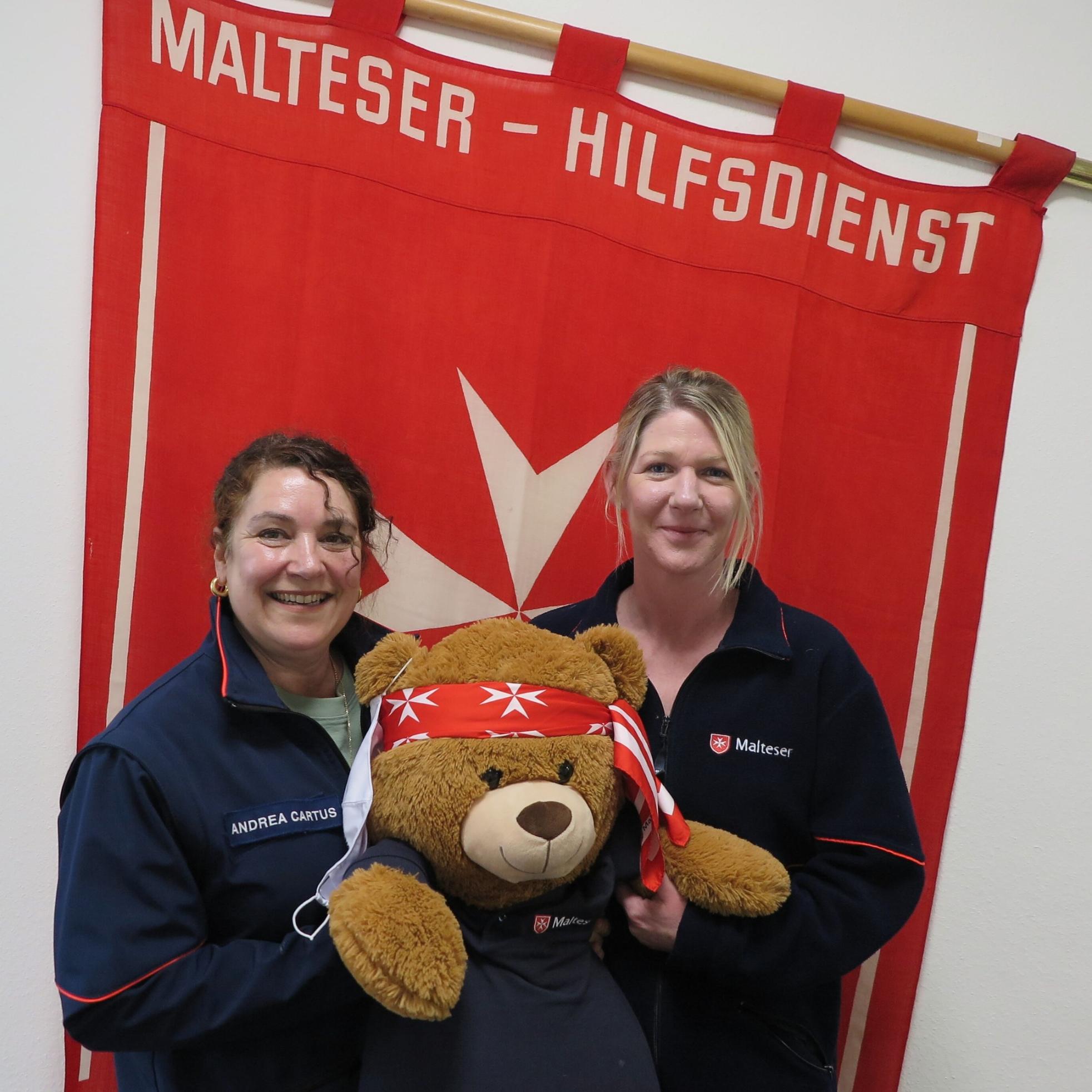 Zwei Frauen in Malteser-Jacken halten einen Teddybär