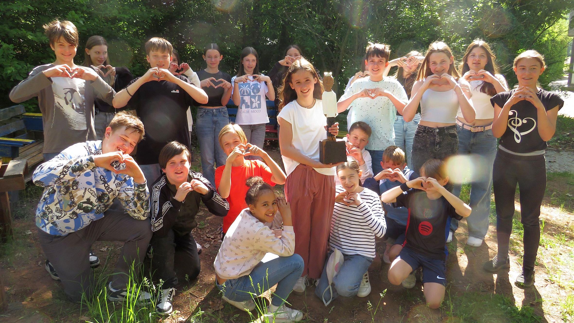 Eine Gruppe Schüler formt mit den Händen ein Herz, in der Mitte eine Königsfigur