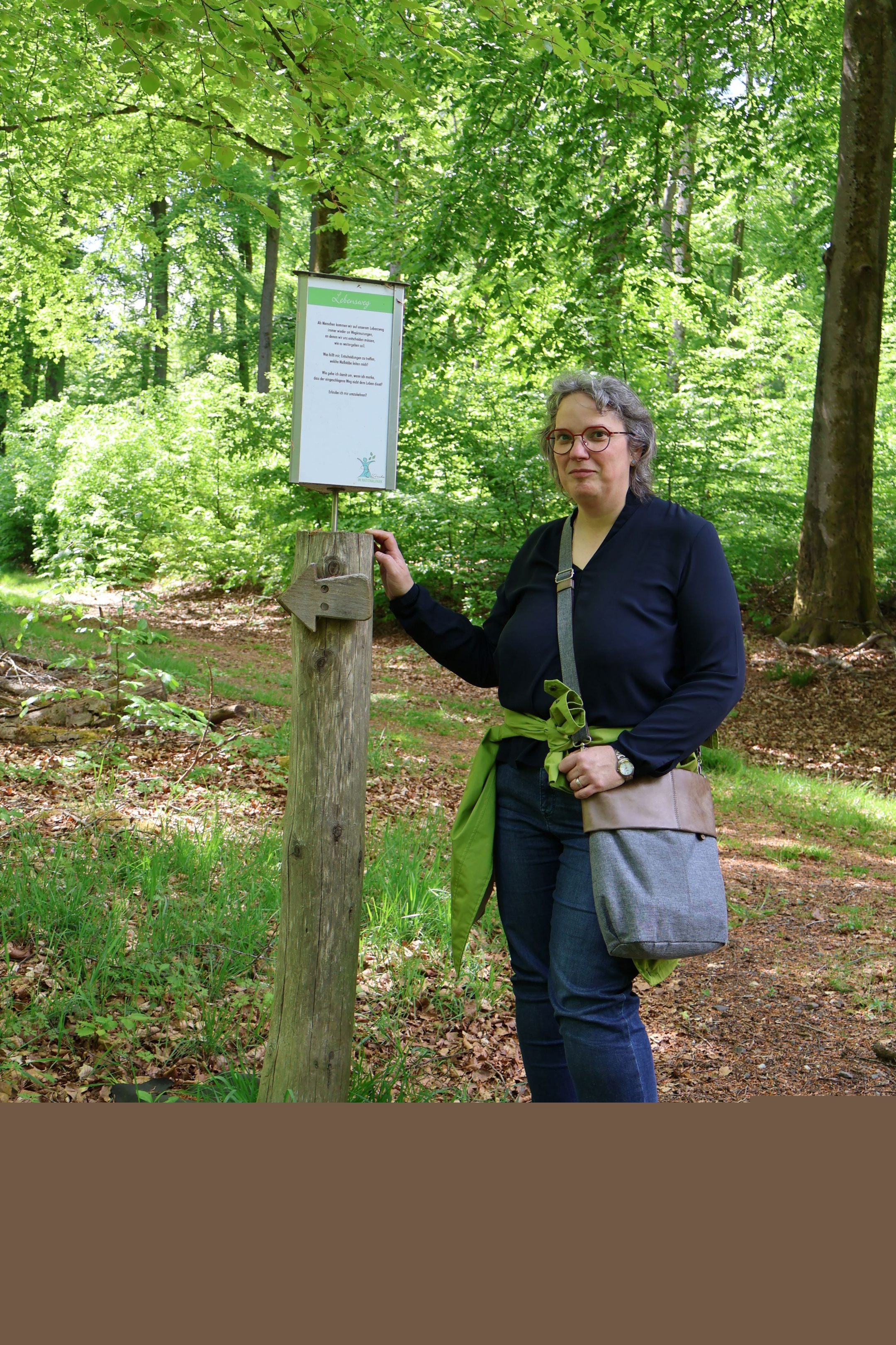Eine Frau zeigt im Wald auf ein Schild an einem Baum (c) Gaby Jacquemoth Eine Frau zeigt im Wald auf ein Schild an einem Baum