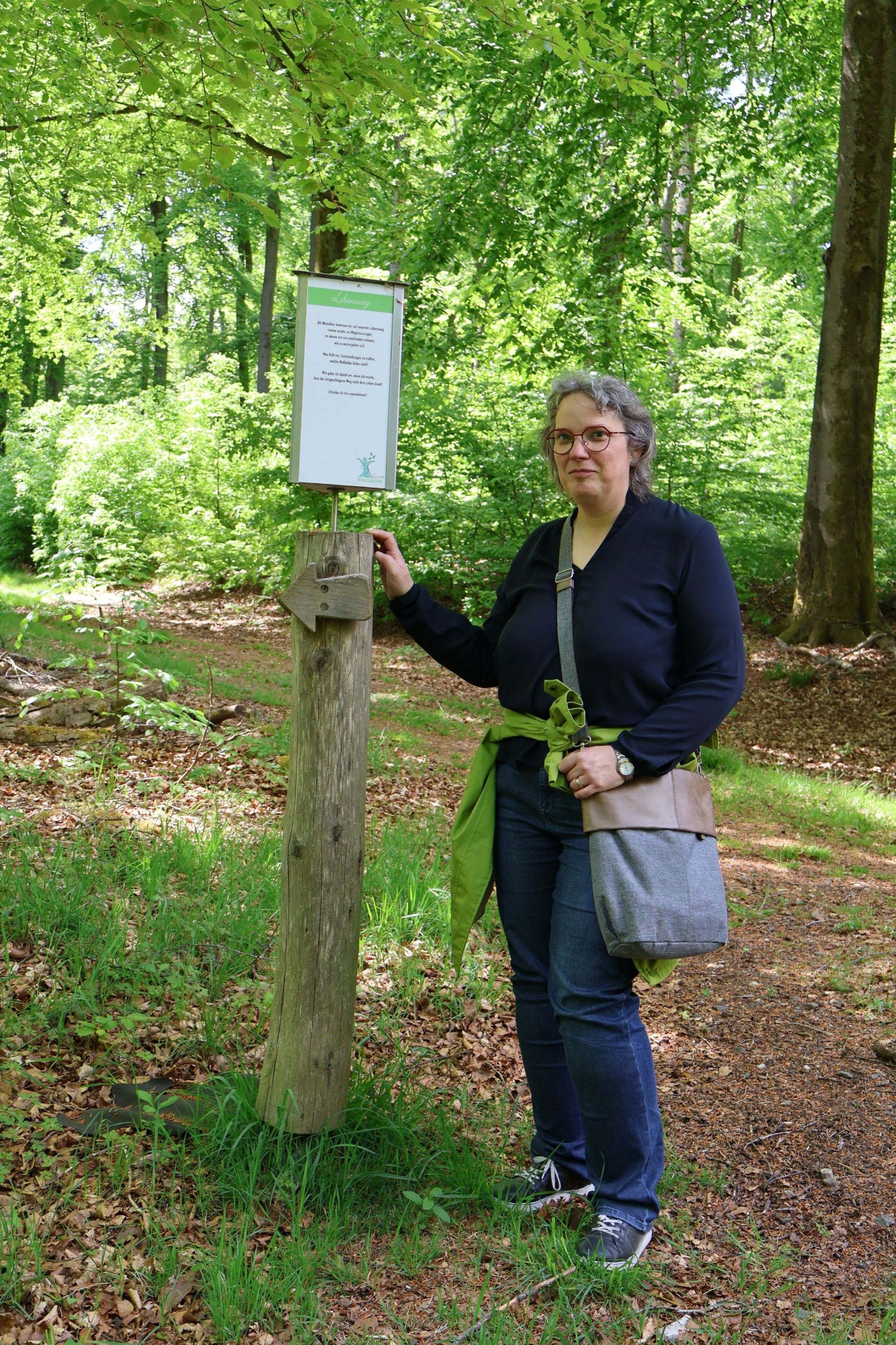 Eine Frau zeigt im Wald auf ein Schild an einem Baum