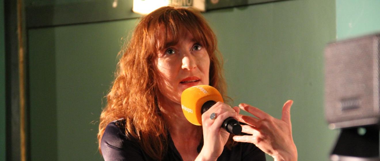 Eine junge Frau mit rötlichen Haaren sitzt vor einem Mikro
