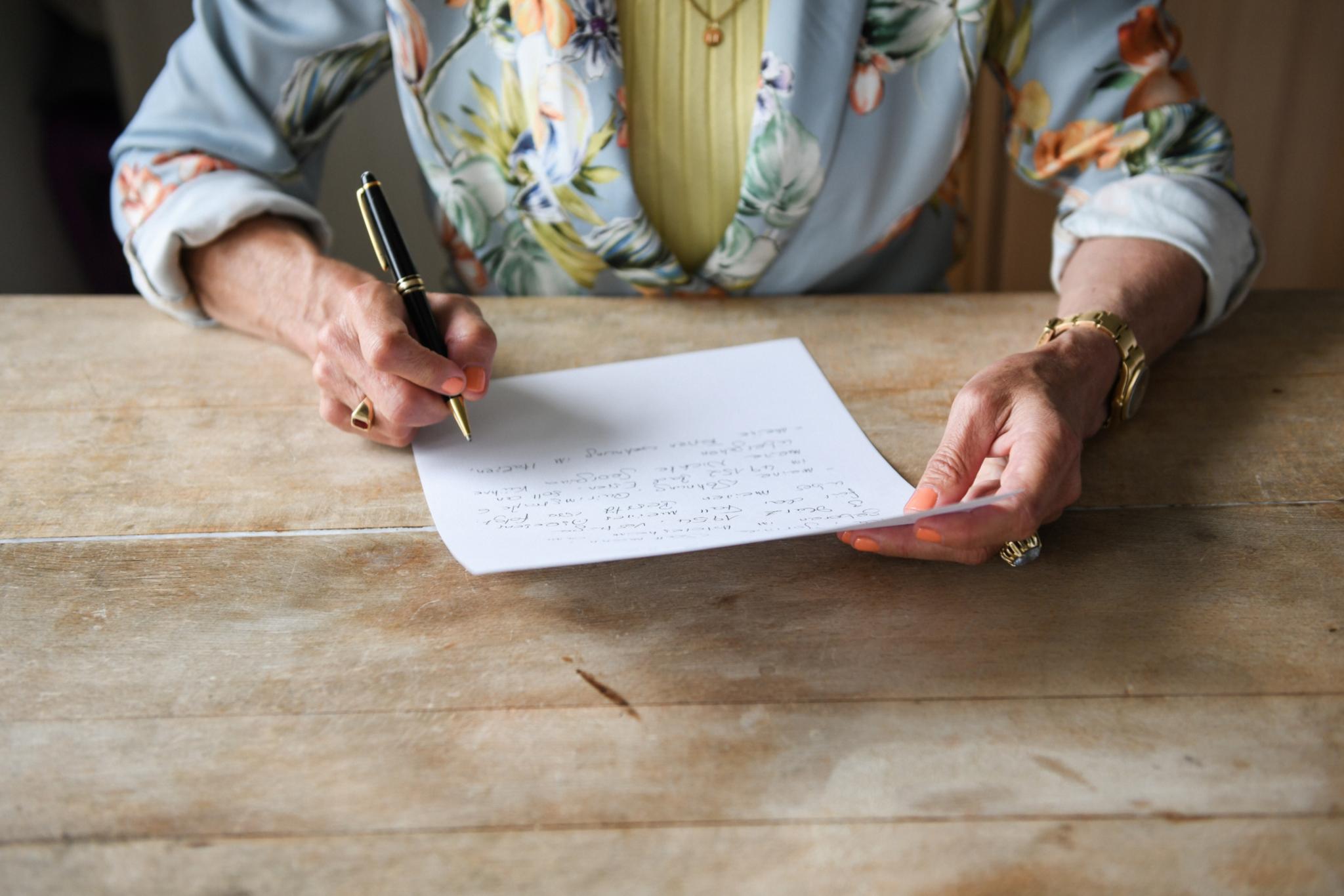 Frauenhände halten einen Papierbogen. Die Frau schreibt ihren handschriftlich formulierten letzten Willen.