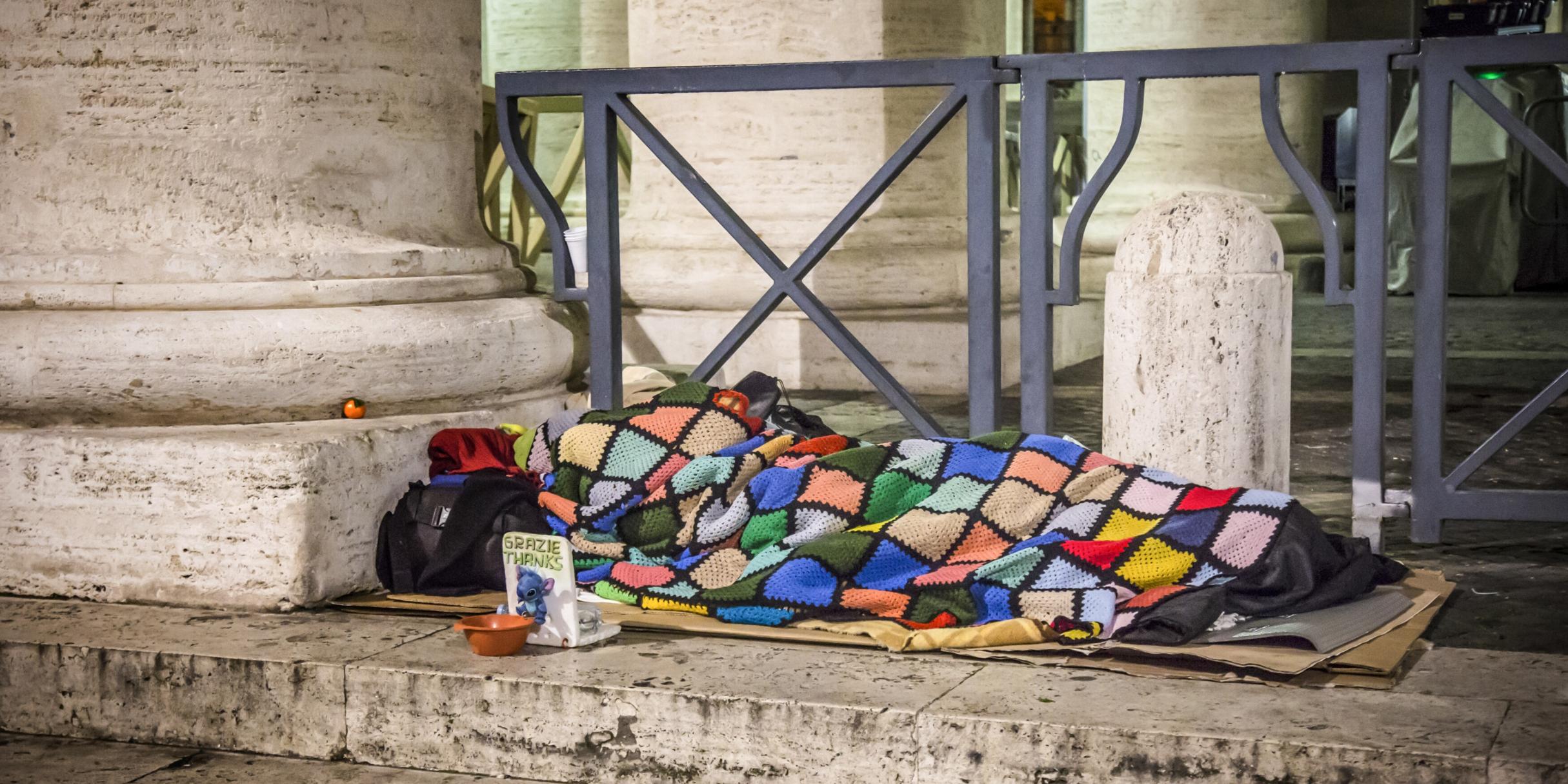 Ein Obdachloser schläft am 10. Januar 2017 auf Pappkartons unter einer bunten Decke auf dem Boden unter den Bernini-Kolonnaden am Petersplatz im Vatikan. Vor ihm steht ein Sammelbecher. (c) KNA Ein Obdachloser schläft am 10. Januar 2017 auf Pappkartons unter einer bunten Decke auf dem Boden unter den Bernini-Kolonnaden am Petersplatz im Vatikan. Vor ihm steht ein Sammelbecher.
