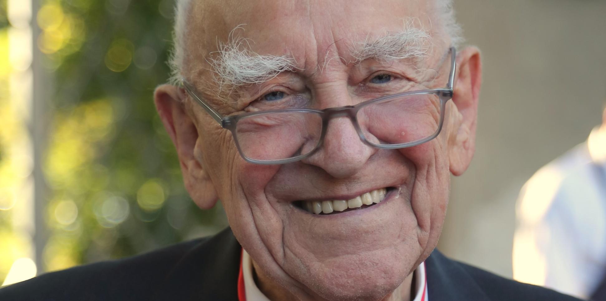 Ein älterer Mann mit einem Orden um den Hals lacht in die Kamera